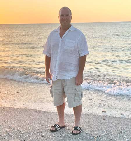 Penn Medicine bariatrics patient Neil Scott stands on a beach at sunset
